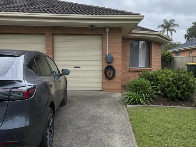 EV charger mounted on a brick garage wall beside a driveway and roller door in Tuggerah