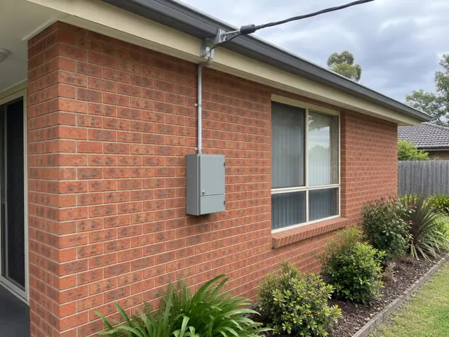 Overhead service cable and point-of-attachment bracket on a brick house exterior in Wyong